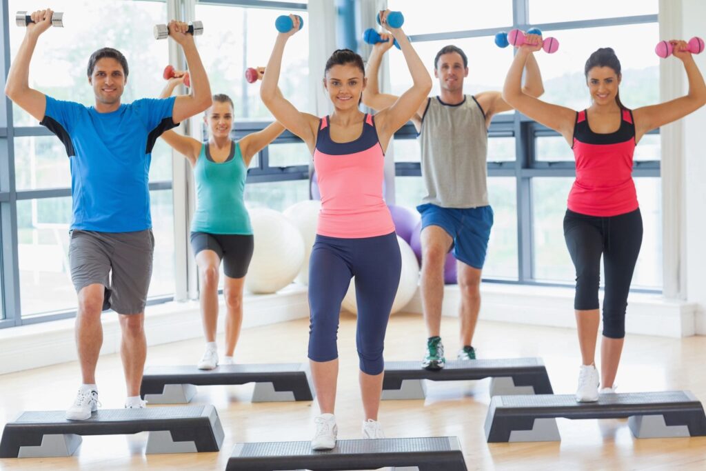 Five people working out together using dumbbells and steps.