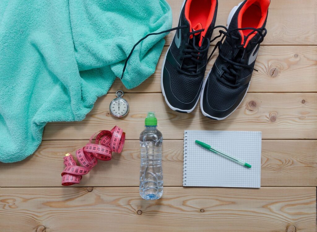 Running shoes, workout journal, water bottle, tape measure, and a towel on the floor.