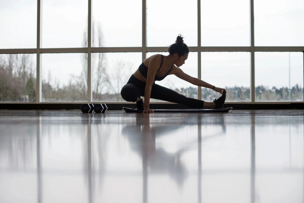 A woman stretching on a mat with glass windows behind her