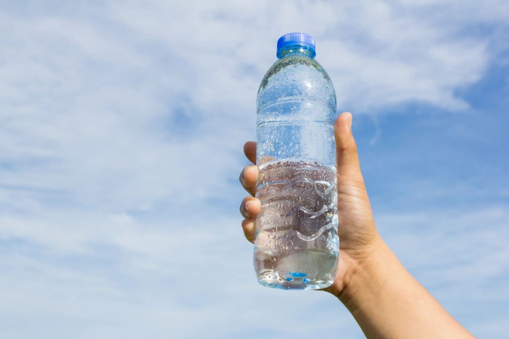 A person holding a bottle of water in front of a cloudy sky.