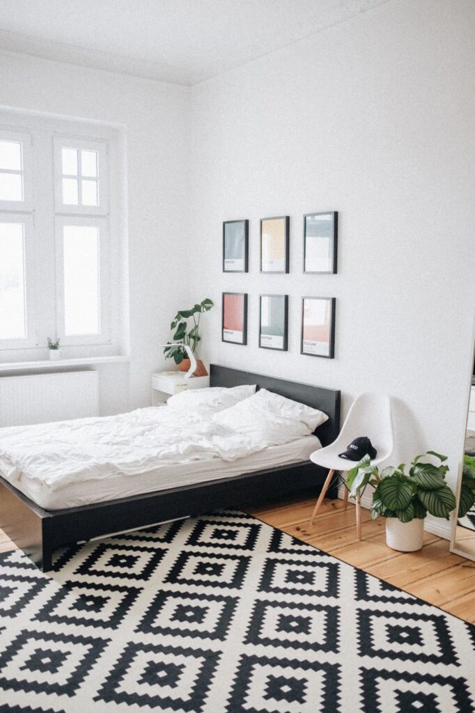 A bedroom with a bed, black and white rug, green plant, and six pictures on the wall.