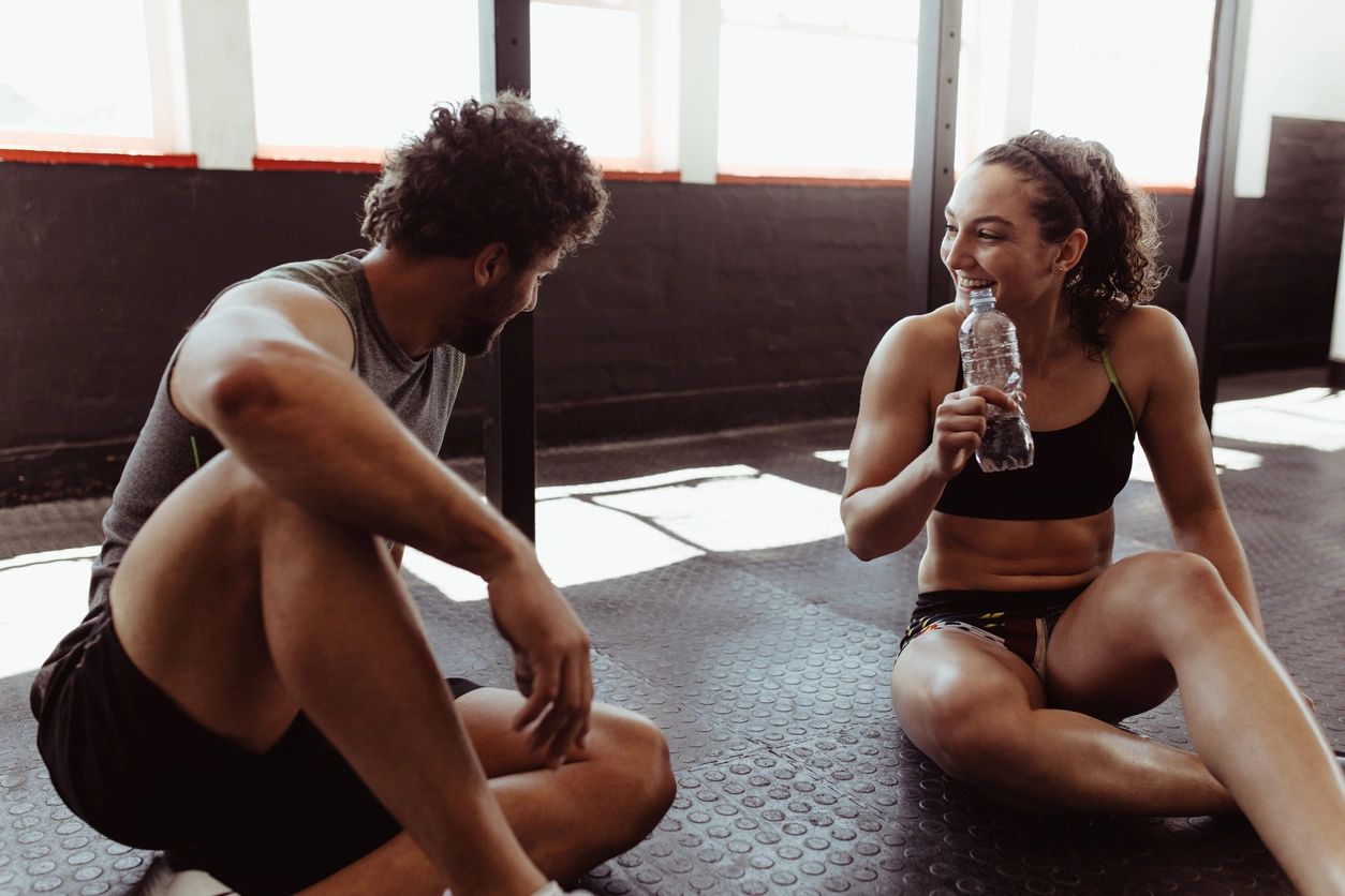 Man and woman at the gym. The woman is drinking water from a bottle.